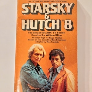May include: A paperback book cover with an orange background featuring the title "Starsky & Hutch #8". The cover features a photo of the two main characters from the TV show, Paul Michael Glaser and David Soul, in a close-up shot. The text on the cover reads "The Smash-hit ABC TV Series Created by William Blinn Another High-voltage Thriller Based on the Script by Ron Friedman Adapted by Max Franklin".