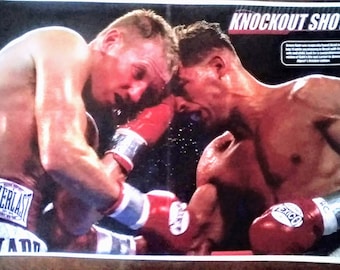 May include: A dynamic image captures a boxing match in action. Two muscular boxers, wearing red gloves, are locked in close combat. The word "EVERLAST" is visible on one boxer's shorts. The image is titled "KNOCKOUT SHOT".