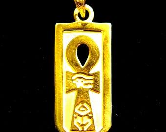 May include: A rectangular gold pendant featuring a white inlay with a raised gold ankh symbol. The ankh is decorated with an Eye of Horus and a smaller hieroglyphic character. The pendant includes a gold bail at the top for attachment to a chain.