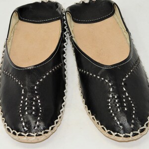Pode incluir: Um par de sapatos pretos de couro sem cadar&ccedil;os com costuras brancas e uma palmilha castanha clara. Os sapatos t&ecirc;m bico arredondado e um padr&atilde;o costurado decorativo na g&aacute;spea.