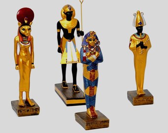 May include: Four gold-colored Egyptian statues on rectangular bases. The statues depict various pharaohs and deities, including a cat-headed figure, a figure holding a staff, and a figure in blue and gold robes. The statues are detailed with black and blue accents.