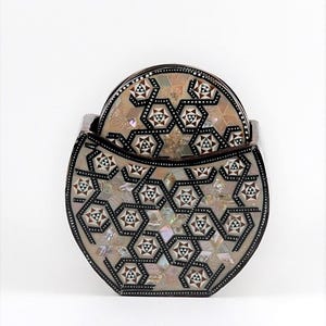 May include: A set of decorative coasters with a matching holder. The coasters and holder feature a geometric pattern with mother-of-pearl and dark brown accents. The holder is oval-shaped and holds several coasters.