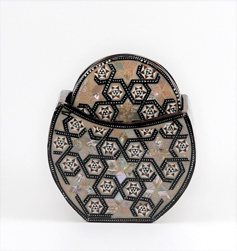 May include: A set of decorative coasters with a matching holder. The coasters and holder feature a geometric pattern with mother-of-pearl and dark brown accents. The holder is oval-shaped and holds several coasters.