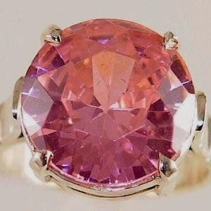 May include: A large, faceted pink gemstone ring with a silver band. The gemstone is a vibrant pink with multiple facets, reflecting light. The ring has a classic design, suitable for various occasions.