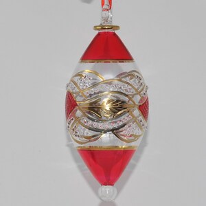 May include: A clear glass Christmas bauble with a red and gold design. The bauble is shaped like a teardrop and has a gold trim around the top.