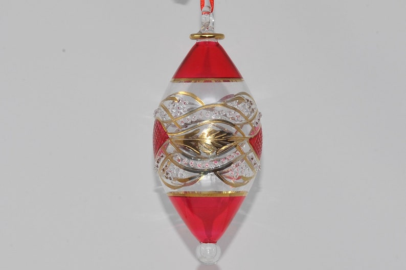 May include: A clear glass Christmas bauble with a red and gold design. The bauble is shaped like a teardrop and has a gold trim around the top.