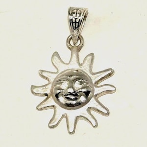 May include: A silver-toned pendant featuring a smiling sun face with radiating rays. The pendant has a detailed bail for attaching to a chain. The sun's face is in the center, with a smiling expression.