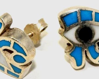 May include: A pair of silver-toned stud earrings. Each earring is in the shape of an eye, with a white iris, a black pupil, and blue mosaic-style accents. The earrings have a post and butterfly backing.