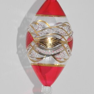 May include: A red and gold glass Christmas bauble with a white and gold swirl design. The bauble has a small loop at the top for hanging.