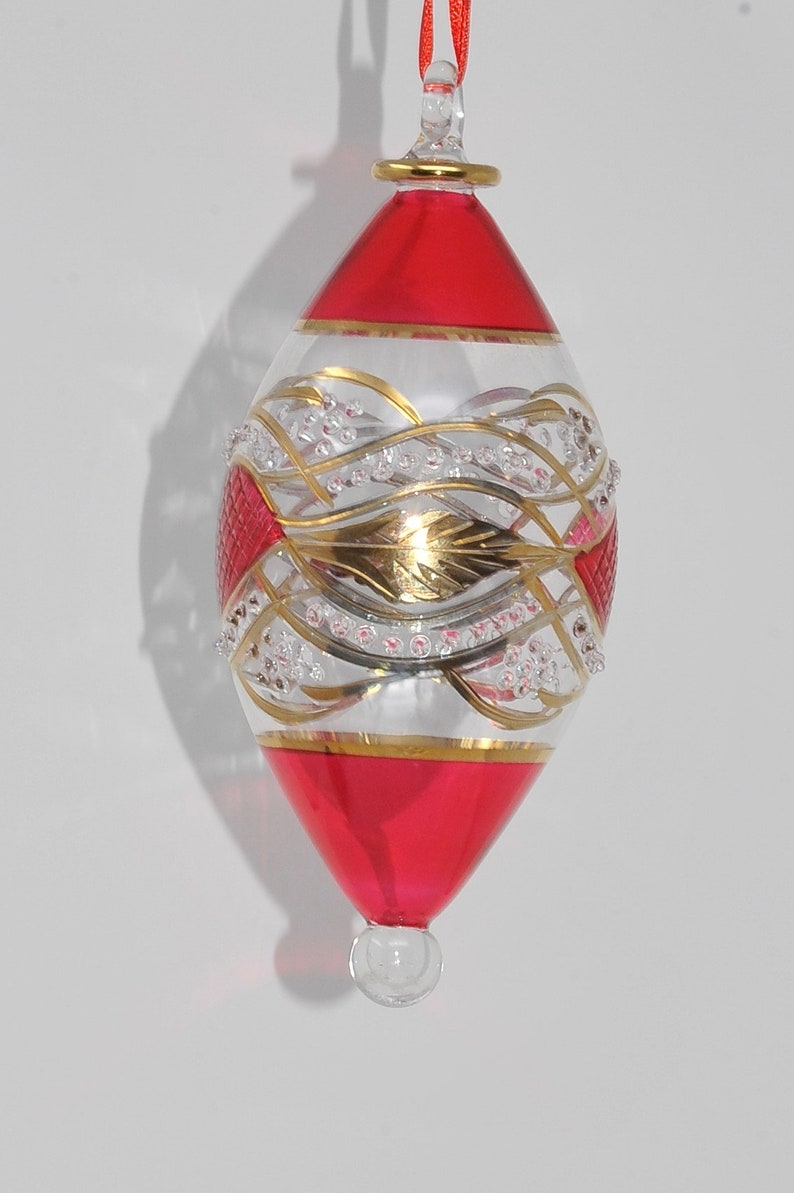 May include: A red and gold glass Christmas bauble with a white and gold swirl design. The bauble has a small loop at the top for hanging.