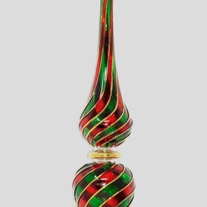 May include: A festive Christmas tree topper in red, green, and gold. The glass ornament features a spiral design with red and green stripes, and gold detailing. The base is a round shape with a gold rim.