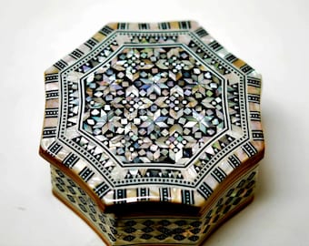 May include: An octagonal decorative box with a mother-of-pearl inlaid lid. The lid features a geometric star pattern in black, white, and iridescent colors. The sides of the box are adorned with a repeating pattern of black and white geometric shapes.