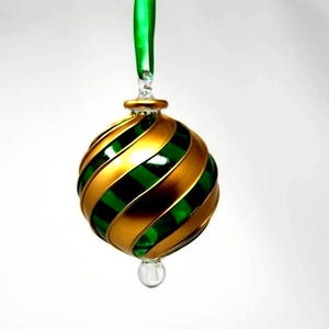 Puede incluir: Un adorno navideño decorativo con un diseño en espiral. El adorno presenta bandas alternas de oro y verde. Una cinta verde está unida a la parte superior para colgarlo. El adorno tiene una lágrima de cristal transparente en la parte inferior.