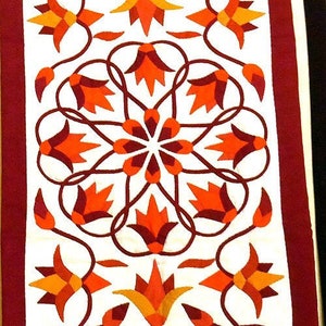 Puede incluir: Un tapiz de pared de tela blanca con un borde burdeos. La tela está decorada con un patrón repetitivo de flores estilizadas de color naranja, rojo y marrón.