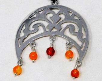 May include: Silver-tone pendant with a crescent moon design. The pendant features intricate cut-out patterns and is adorned with five dangling orange and red beads. The pendant has a loop at the top for a chain.