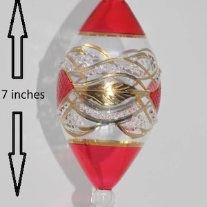 May include: A red and gold glass Christmas bauble with a white and gold design. The bauble is 7 inches tall.