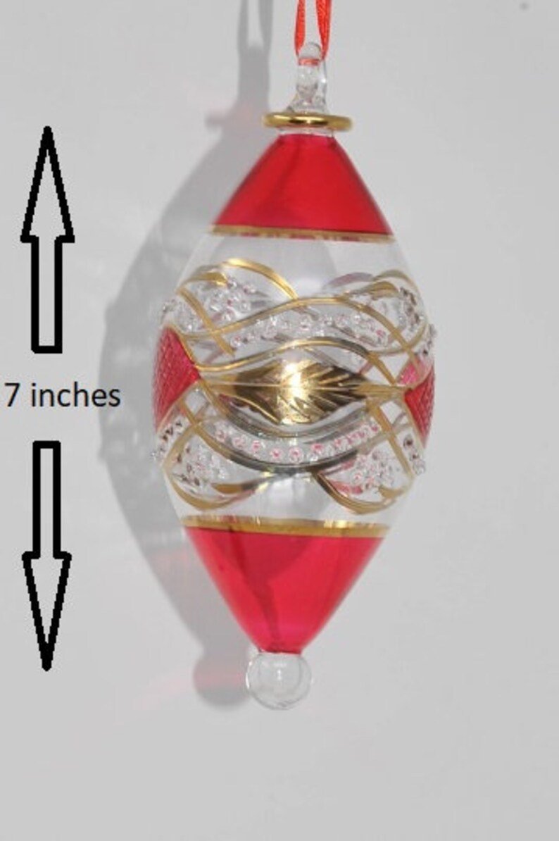 May include: A red and gold glass Christmas bauble with a white and gold design. The bauble is 7 inches tall.