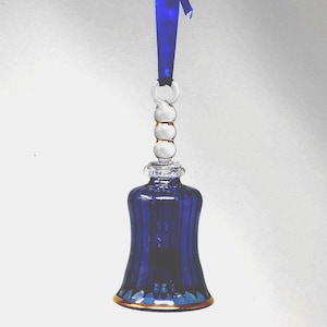 May include: A cobalt blue glass bell ornament with a gold rim and a blue ribbon for hanging. The bell has vertical ridges and a clear glass handle with gold accents. A decorative holiday item.