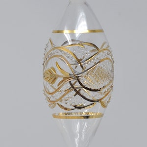 May include: A clear glass Christmas bauble with gold leaf detailing. The bauble features a delicate, intricate design of swirling lines and leaves.
