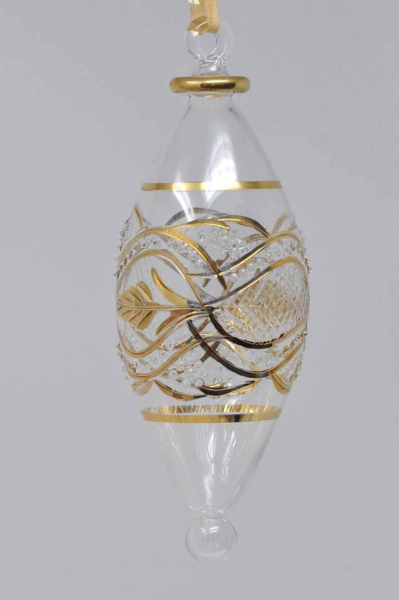 May include: A clear glass Christmas bauble with gold leaf detailing. The bauble features a delicate, intricate design of swirling lines and leaves.