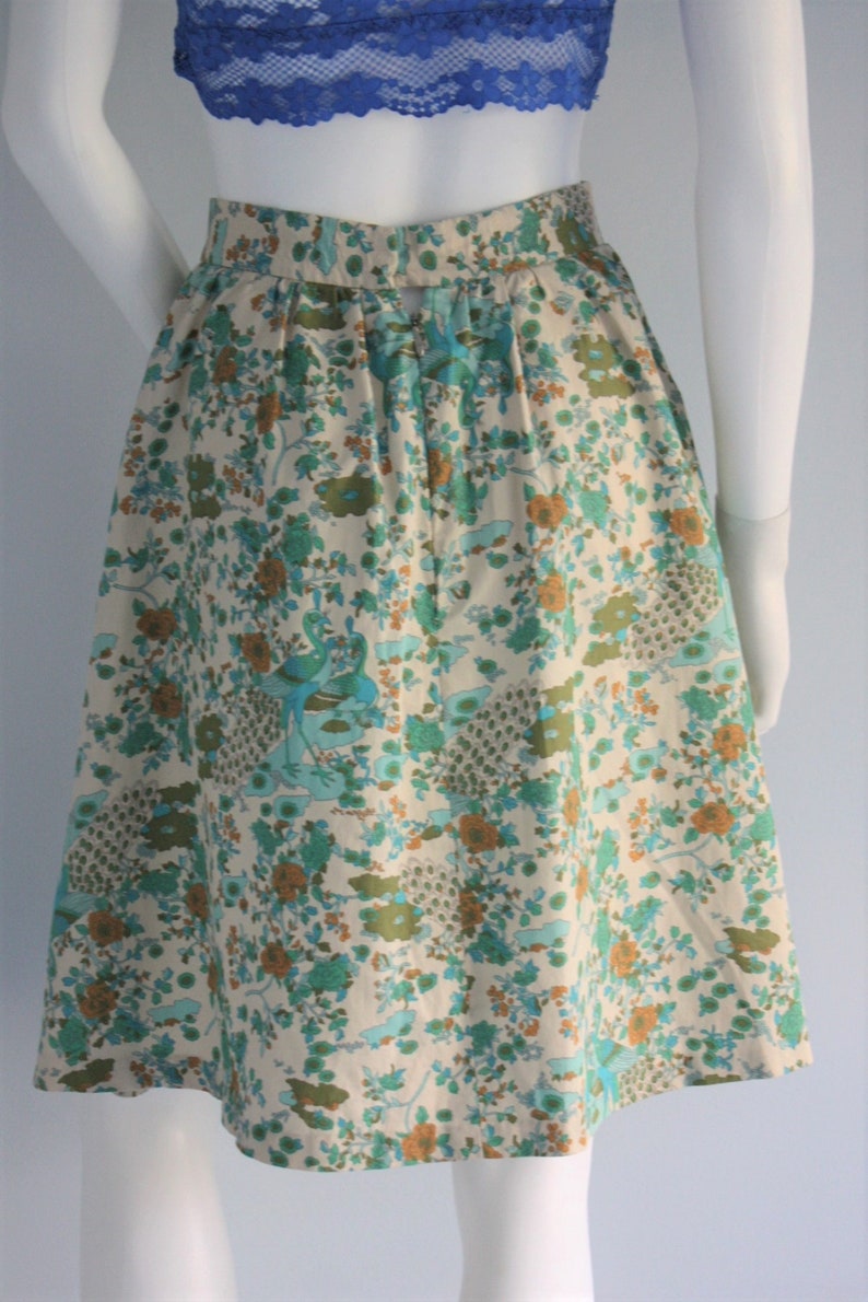 May include: A white skirt with a floral print featuring peacocks and flowers in shades of blue, green, and orange.