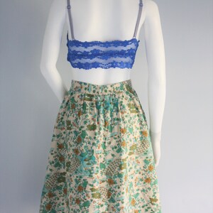 May include: A white skirt with a floral print featuring blue, green, and orange flowers. The skirt has a back zipper closure and a gathered waist.