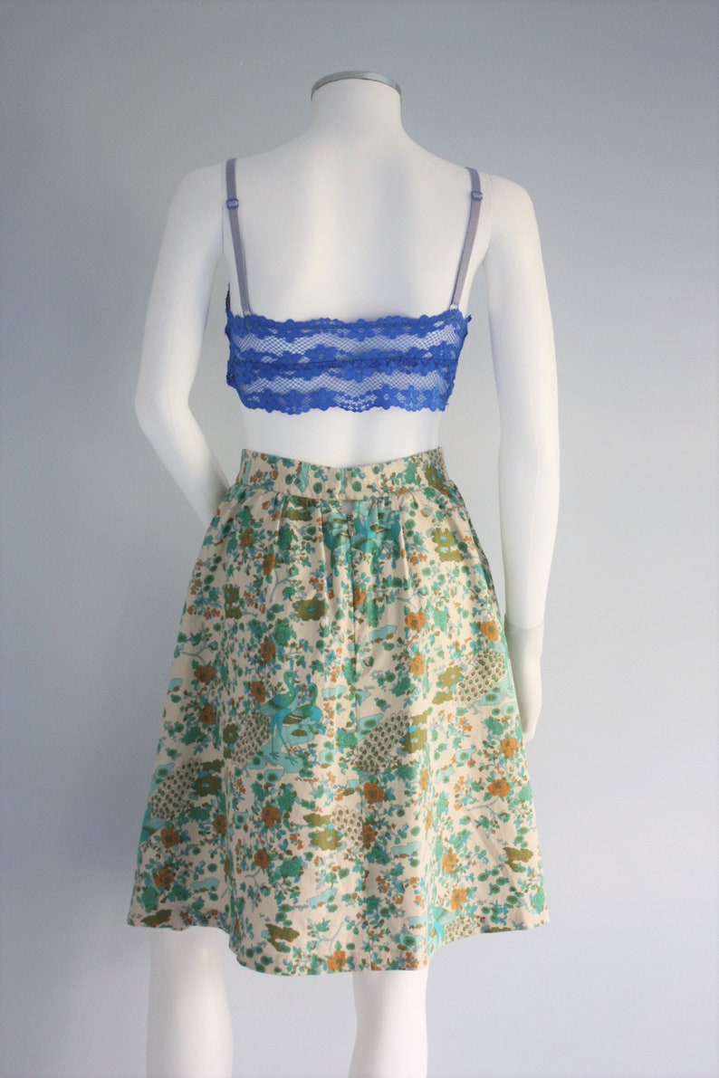 May include: A white skirt with a floral print featuring blue, green, and orange flowers. The skirt has a back zipper closure and a gathered waist.