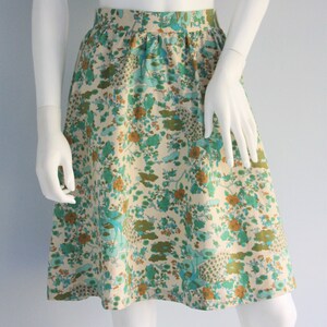 May include: A cream-colored skirt with a floral print featuring green, blue, and orange flowers. The skirt has a gathered waist and a flared silhouette.