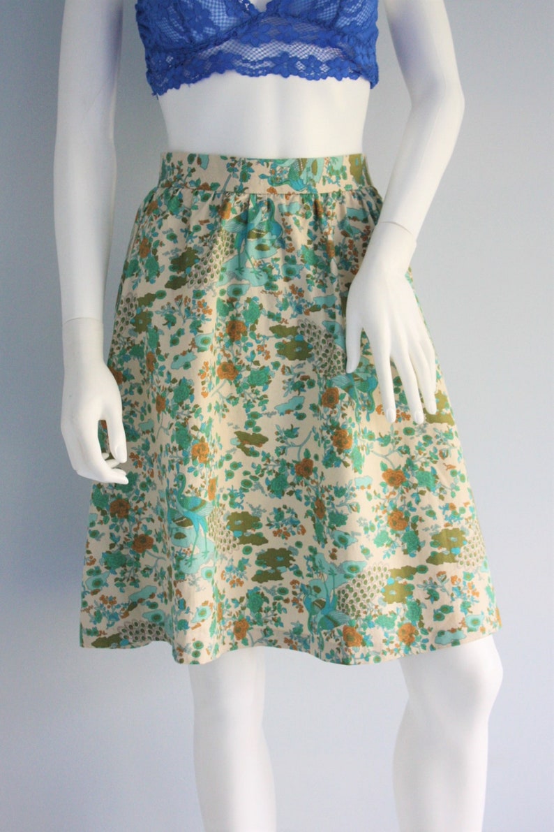May include: A cream-colored skirt with a floral print featuring green, blue, and orange flowers. The skirt has a gathered waist and a flared silhouette.