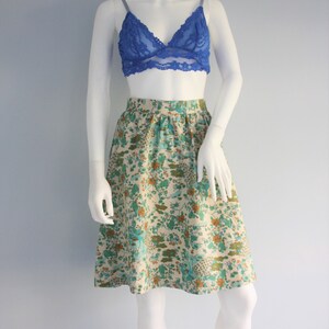 May include: A floral print skirt with a cream background and blue, green, and orange flowers. The skirt is knee-length and has a gathered waist.