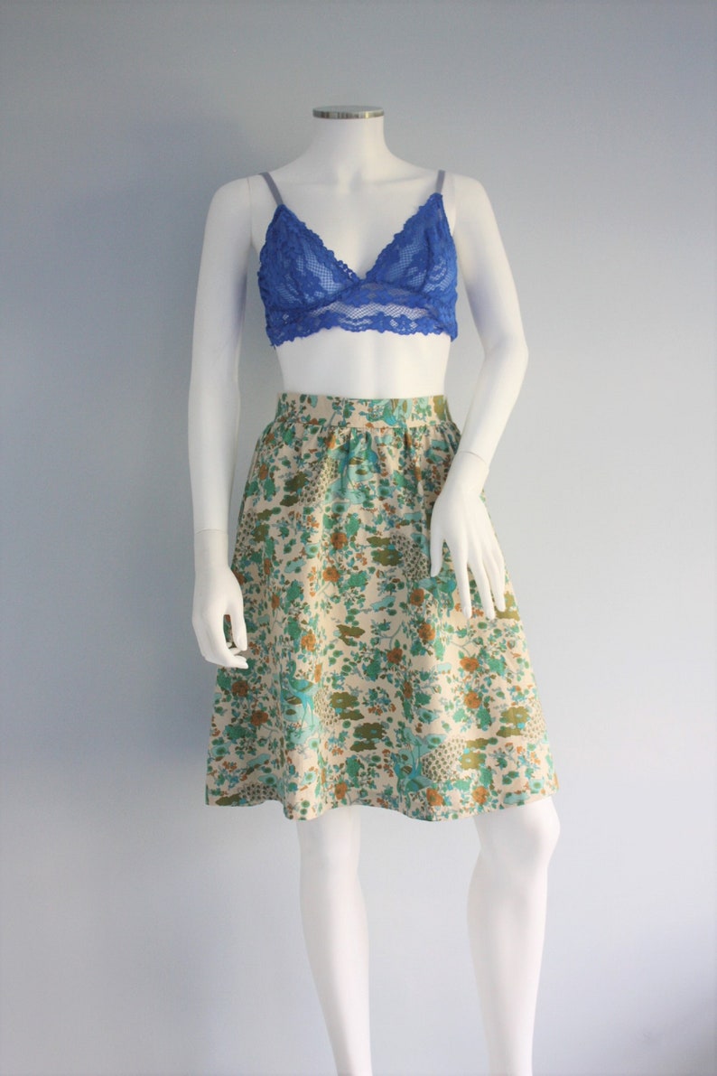 May include: A floral print skirt with a cream background and blue, green, and orange flowers. The skirt is knee-length and has a gathered waist.
