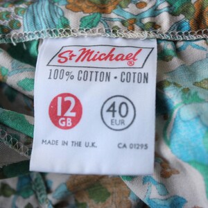 May include: A white tag with black text that reads "St. Michael 100% Cotton - Coton" and has two red circles with the text "12 GB" and "40 EUR". The tag also reads "Made in the U.K. CA 01295".