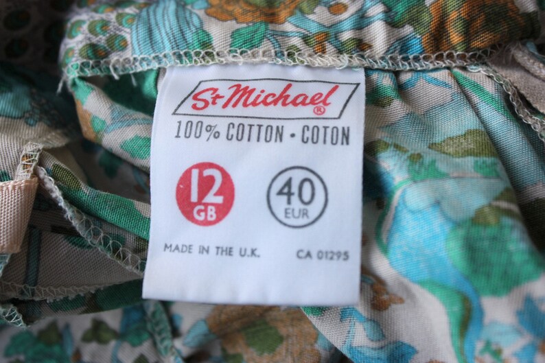 May include: A white tag with black text that reads "St. Michael 100% Cotton - Coton" and has two red circles with the text "12 GB" and "40 EUR". The tag also reads "Made in the U.K. CA 01295".