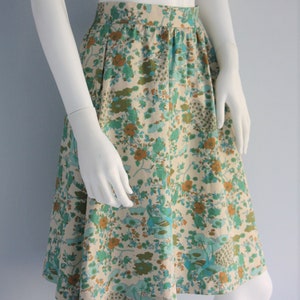 May include: A white skirt with a floral print in shades of blue, green, and brown. The skirt has a fitted waist and a flared hem.
