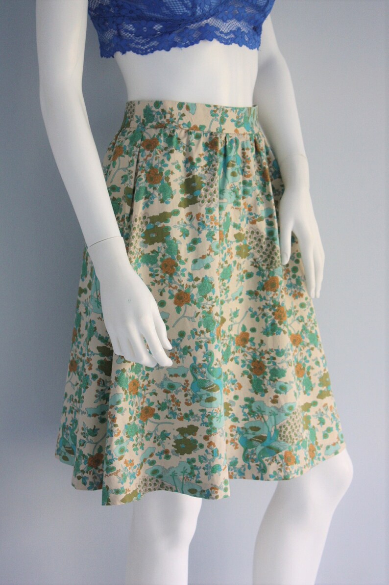 May include: A white skirt with a floral print in shades of blue, green, and brown. The skirt has a fitted waist and a flared hem.