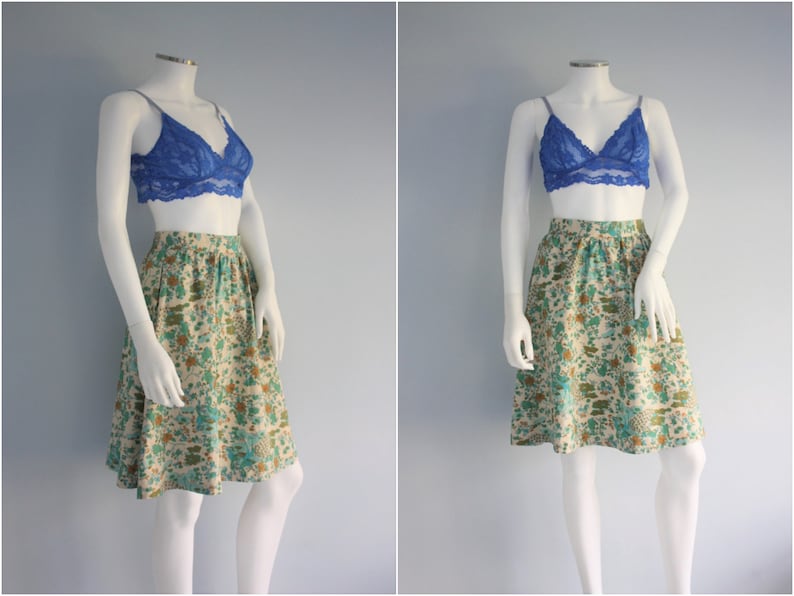 May include: A white skirt with a floral print in shades of green, brown, and blue. The skirt has a fitted waist and a flared hem. It is paired with a blue lace bralette.