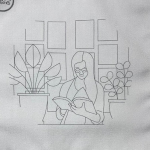 May include: White square fabric with a line drawing of a person reading a book, wearing glasses, and surrounded by potted plants. The fabric has a logo in the upper left corner that says "Cori Crafts".