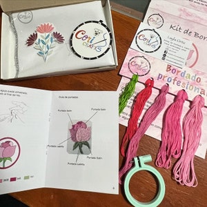 Puede incluir: Kit de bordado con diseño floral, que incluye hilo, un bastidor e instrucciones. El kit presenta una tela blanca con un colorido estampado floral, varios ovillos de hilo en tonos rosas y verdes, y un bastidor de bordado verde menta. Cori Crafts.