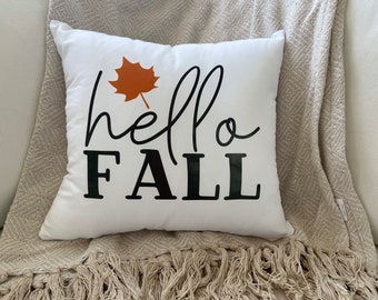 May include: White throw pillow with a black and orange design. The pillow has the text "hello fall" with a stylized orange leaf.
