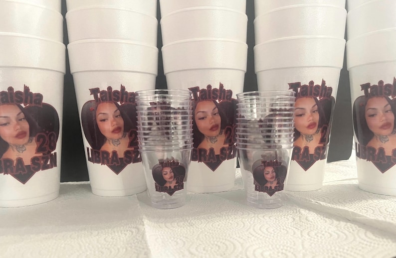 Puede incluir: Vasos de espuma blancos y vasos de pl&aacute;stico transparente con un dise&ntilde;o impreso. El dise&ntilde;o presenta la cara de una mujer, el nombre "Taisha", el n&uacute;mero "28" y las palabras "Libra Szn" en un gr&aacute;fico en forma de coraz&oacute;n.