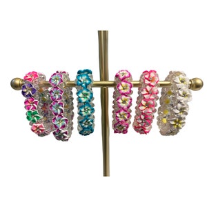 May include: Six colorful flower bracelets on a gold stand. The bracelets are made of white beads with colorful flowers.