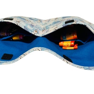 Puede incluir: Una bolsa de tela azul y blanca con un patr&oacute;n de copo de nieve y un forro de franela azul. La bolsa est&aacute; abierta y tiene dos compartimentos, cada uno con cintas de colores.