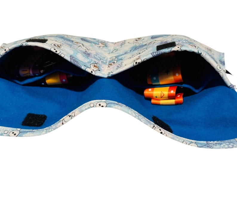 Puede incluir: Una bolsa de tela azul y blanca con un patr&oacute;n de copo de nieve y un forro de franela azul. La bolsa est&aacute; abierta y tiene dos compartimentos, cada uno con cintas de colores.