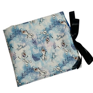 Puede incluir: Una bolsa de tela azul y blanca con un lazo negro. La bolsa presenta un patr&oacute;n repetido de Olaf de la pel&iacute;cula Frozen, con el texto "Ice Breaker!" repetido en toda la superficie.