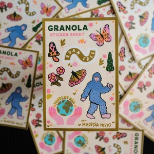 May include: A collection of "Granola Sticker Sheet" featuring whimsical illustrations. The stickers include a blue Bigfoot, butterflies, mushrooms, flowers, and the text "Roam Free" and "Protect Her". The artist's name, Marissa Nieto, is also included.