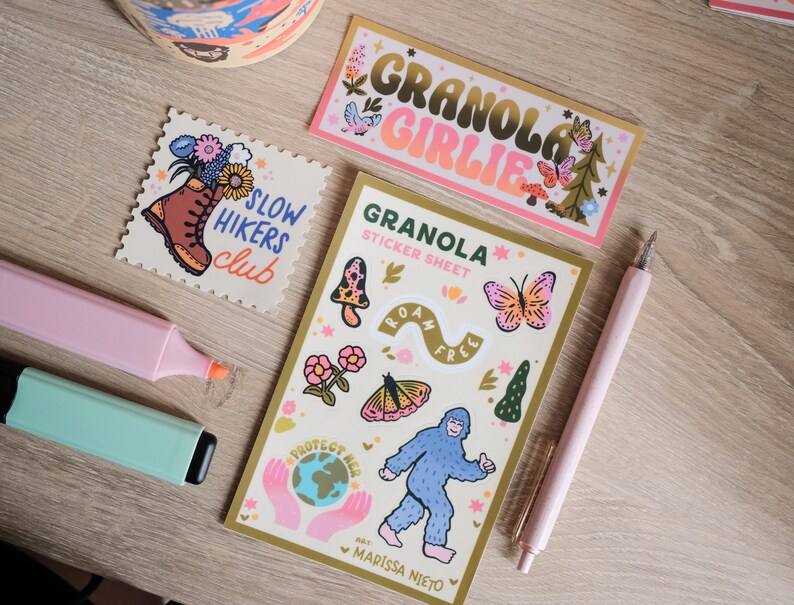 May include: A collection of stickers and stationery items, including a sticker sheet with a Bigfoot illustration, a sticker that says "Granola Girlie", and a sticker with a hiking boot and flowers. Also included are two highlighters and a pink pen.
