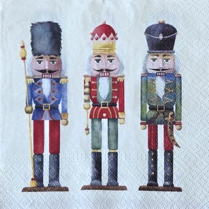 May include: Three decorative nutcracker figures on a white background. The nutcrackers are dressed in colorful military-style uniforms with hats and are holding staffs or swords. The figures are painted in shades of blue, red, green, and gold.