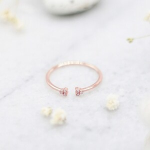 May include: A delicate rose gold ring with two open ends, each adorned with three small sparkling diamonds.