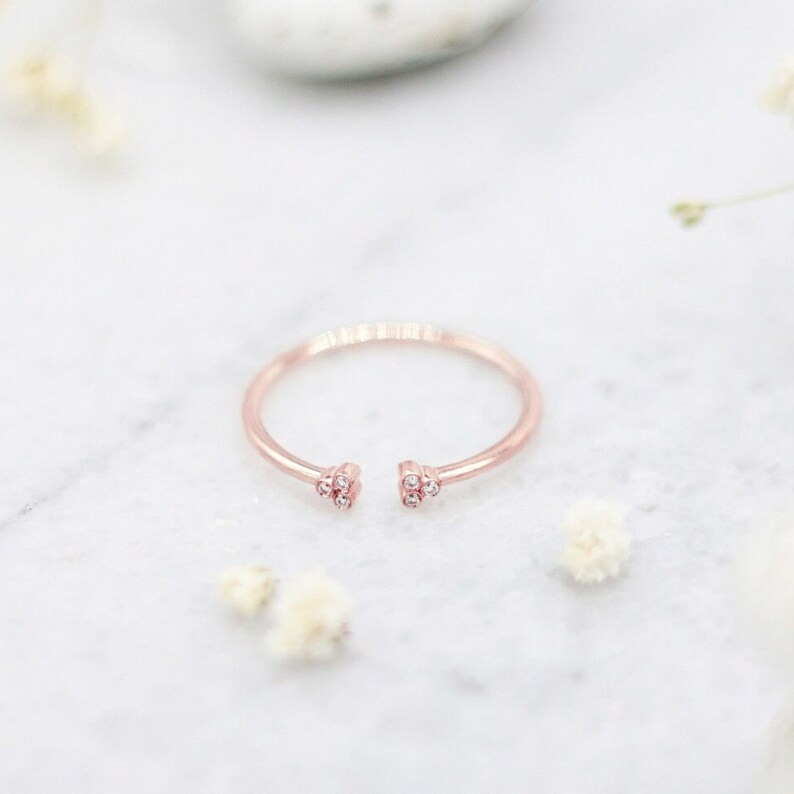 May include: A delicate rose gold ring with two open ends, each adorned with three small sparkling diamonds.