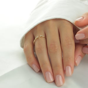 May include: A gold ring with two small diamonds on the ends. The ring is open and sits on a finger.